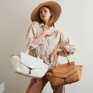 woman holding a white handbag and a tan handbag wearing an oversized hat