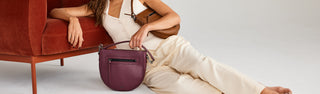 model sitting with beatrice saddle crossbody in malbec and caramel