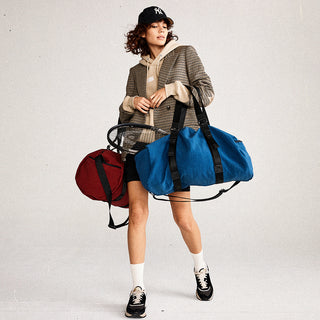 girl holding two duffle bags one in blue one in red